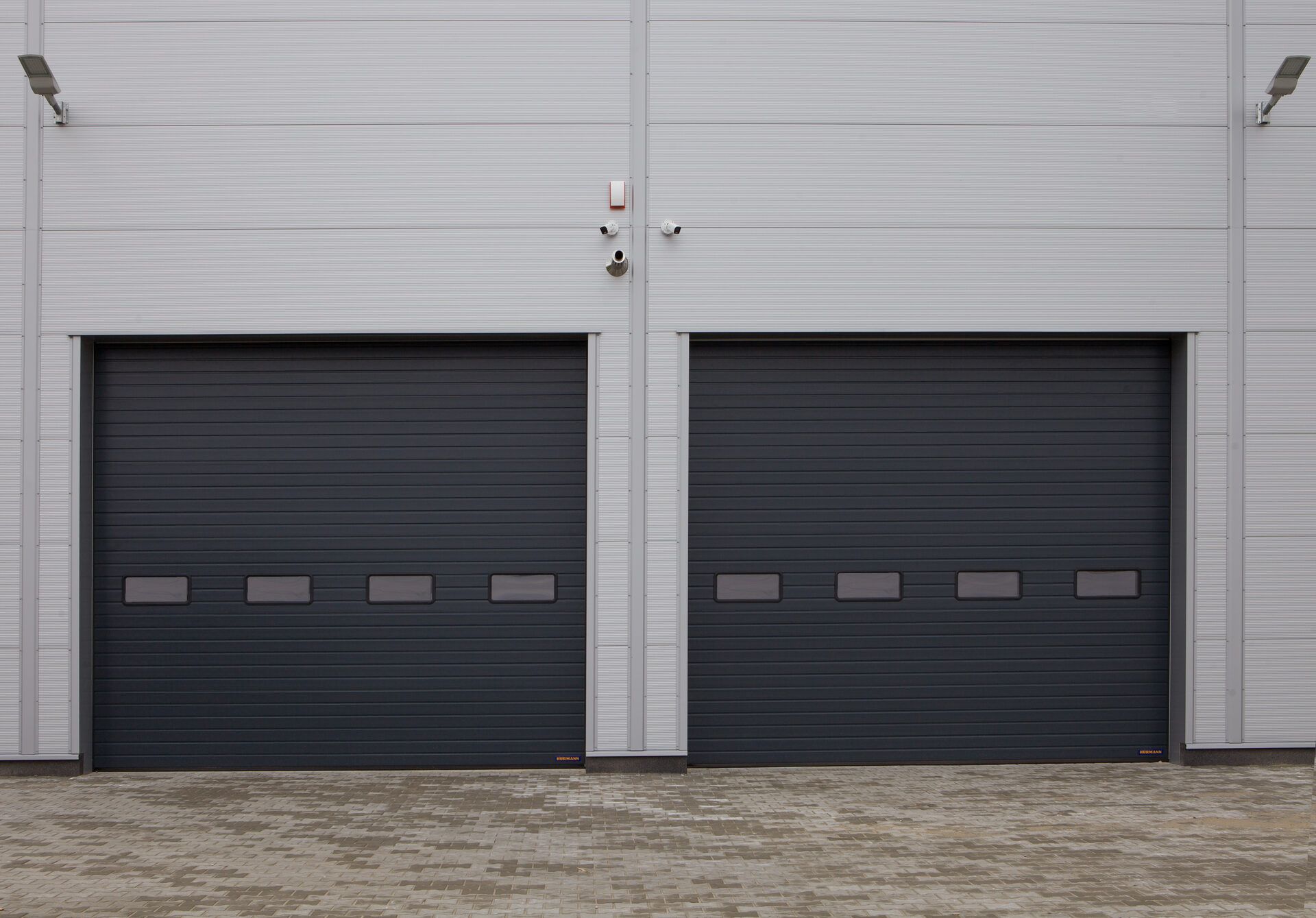 Two large dark commercial sectional garage doors on an industrial building