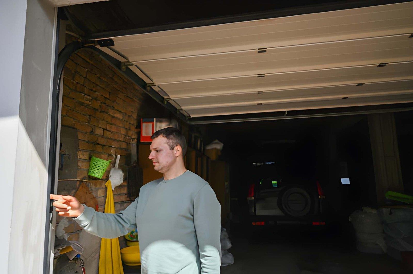 A technician in a grey sweater standing in a garage, pointing at the side of an open garage door.