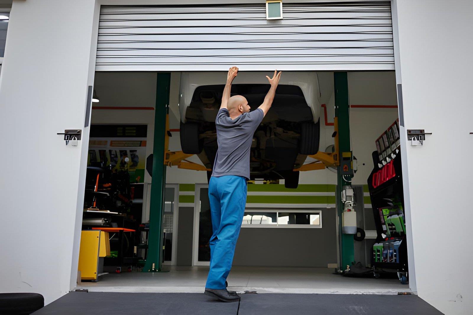 A technician in blue pants and a grey shirt manually lifting a garage door in a workshop.